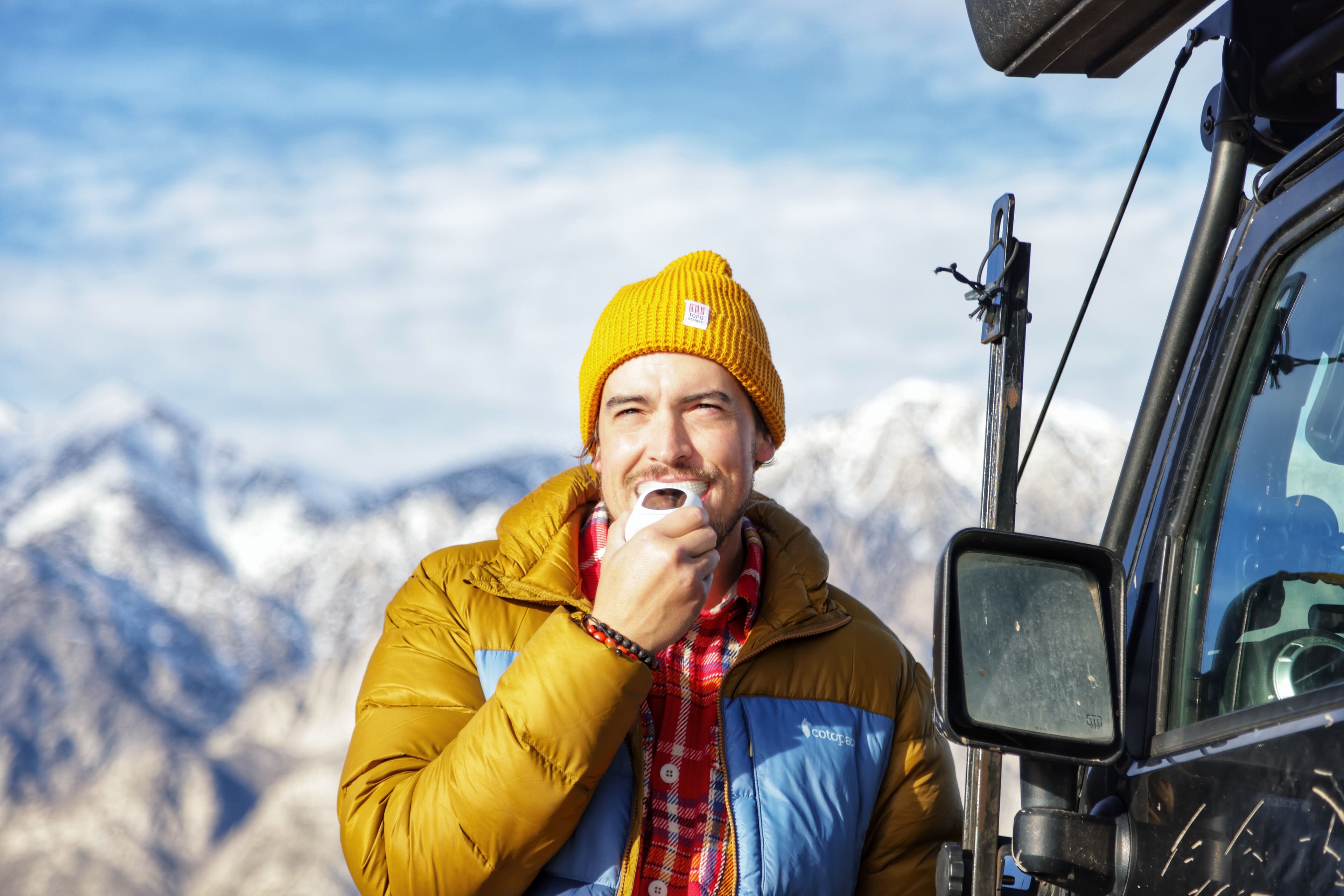 A man cleaning his teeth with the Feno smartbrush outdoors, a mountain range behind him