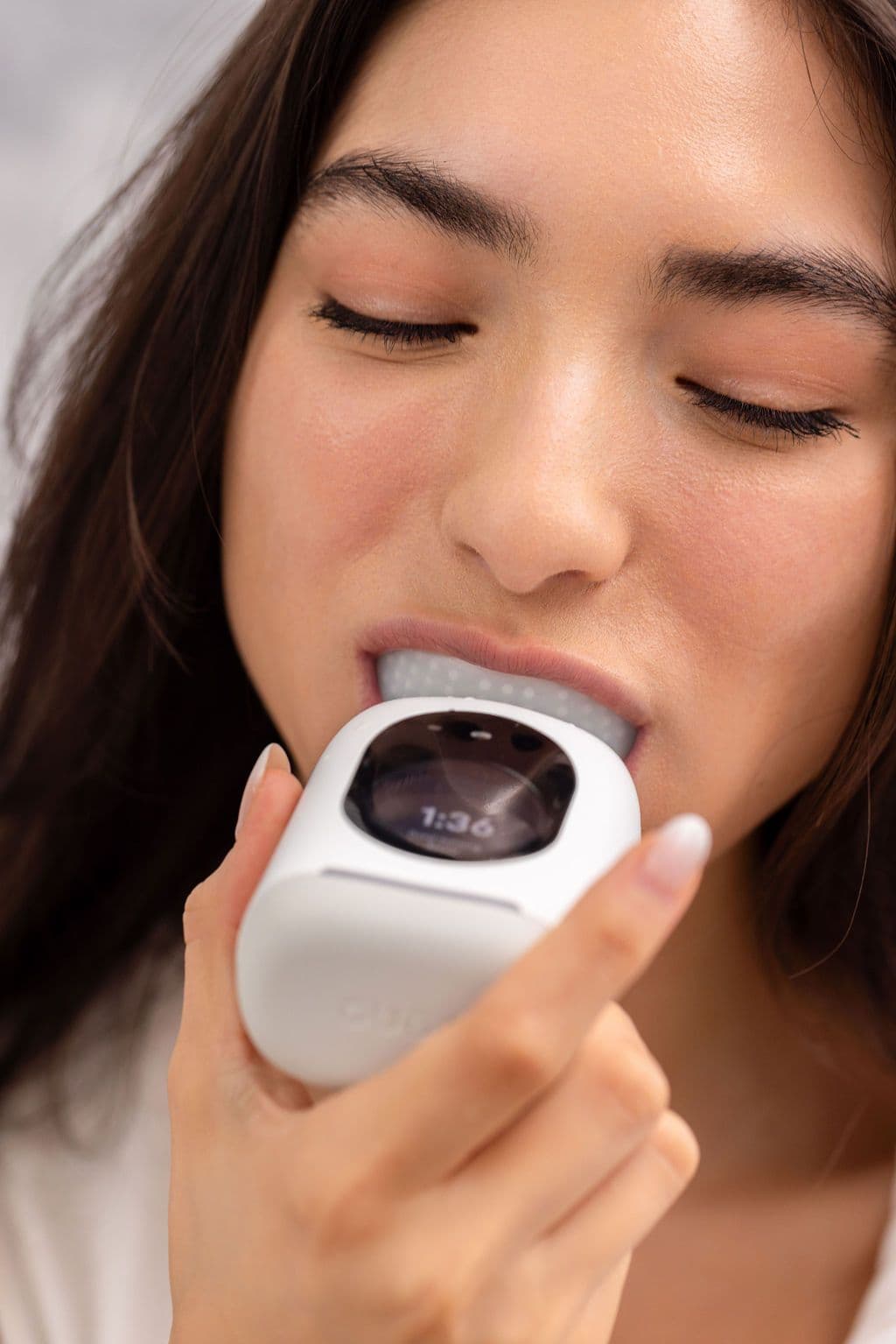 A woman brushing with the Feno smartbrush, the countdown timer visible on the pod's screen